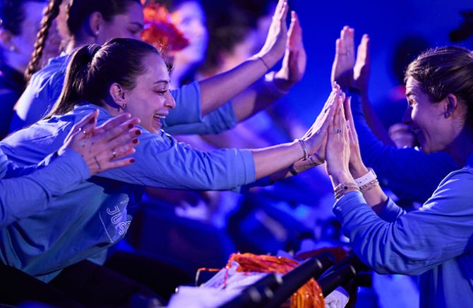People in blue shirts enthusiastically high-five each other in a lively, brightly lit setting.