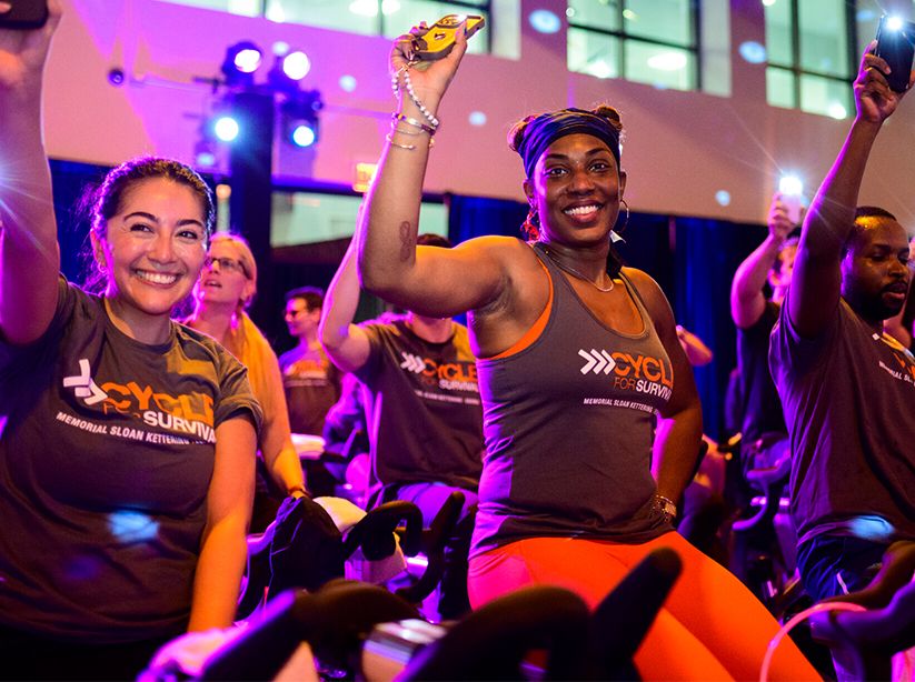 Cyclists smiling and raising hands during an indoor event.