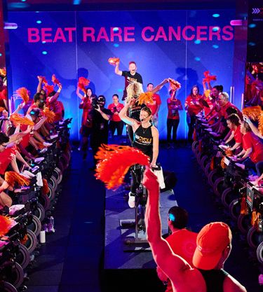 Cycling event with participants in red, raising orange pom-poms, vibrant atmosphere.