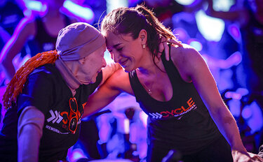 Two women lean their foreheads together during an emotional moment at a Cycle for Survival event.