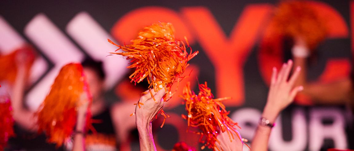 Hands waving orange pom-poms at a Cycle for Survival event for rare cancer research. 