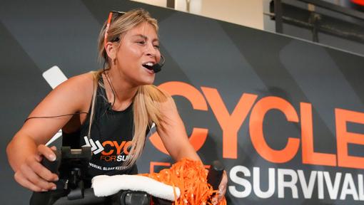 A fitness instructor on a stationary bike leading a Cycle for Survival rare cancer fundraising event in Miami.
