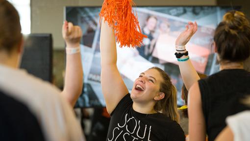 People at a Cycle for Survival rare cancer fundraising event smiling, cheering, and waving orange pom-poms.