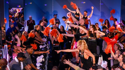 Cycling class with cheering participants and orange pom-poms.