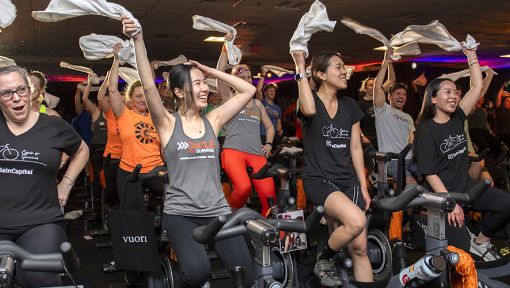 A group of people riding stationary bikes at a Cycle for Survival fundraising ride in Boston.