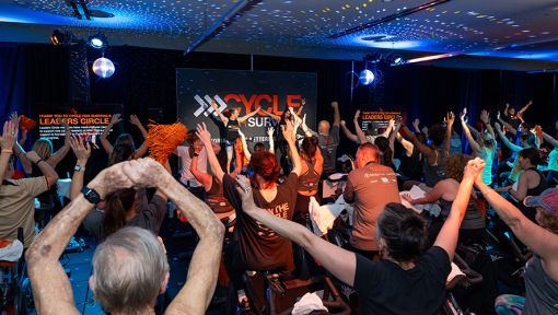 People at a Cycle for Survival rare cancer fundraising event smiling, cheering, and waving orange pom-poms.