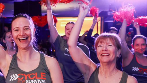 A group of people smile and wave orange pom poms at a Cycle for Survival event.