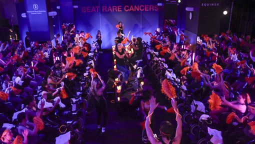 A SoulCycle instructor leading a Cycle for Survival rare cancer fundraising ride surrounded by event participants on stationary bikes.