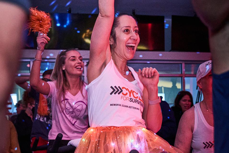 A person cheering on a stationary bike at a Cycle for Survival rare cancer fundraising event in Long Island. 