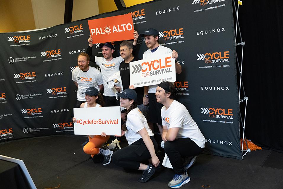 xPeople holding signs and posing for a picture together at a Cycle for Survival rare cancer fundraising event in Palo Alto.  