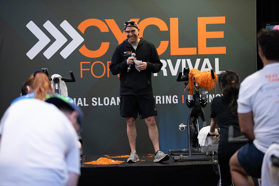 A person standing with a microphone speaking at a Cycle for Survival rare cancer fundraising event in Palo Alto. 