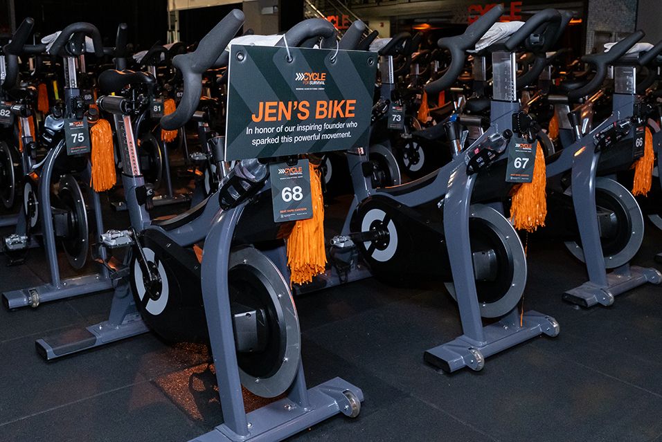 A stationary bike at a Cycle for Survival event bears a sign that reads “Jen’s Bike: In honor of our inspiring founder who sparked this powerful movement.” 