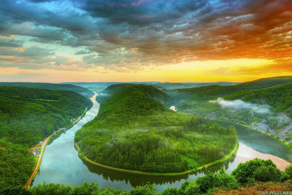River winding through lush green hills at sunrise, colorful sky above.