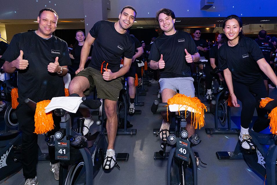 Four Blackstone employees take a break on their stationary bikes at a Cycling for Survival fundraiser for rare cancer research at MSK.