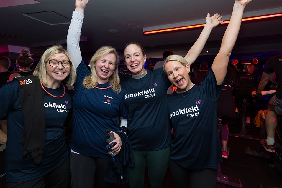 Four Brookfield employees wearing shirts that read “Brookfield Cares” celebrate at a Cycle for Survival fundraiser.