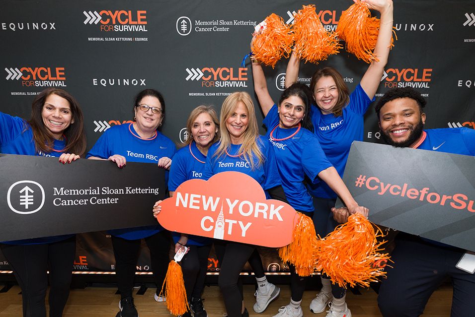 RBC employees gather for a photo in front of a backdrop of Cycle for Survival logos. Some hold signs reading “Memorial Sloan Kettering Cancer Center,” “New York City,” and “#CycleforSurvival.”