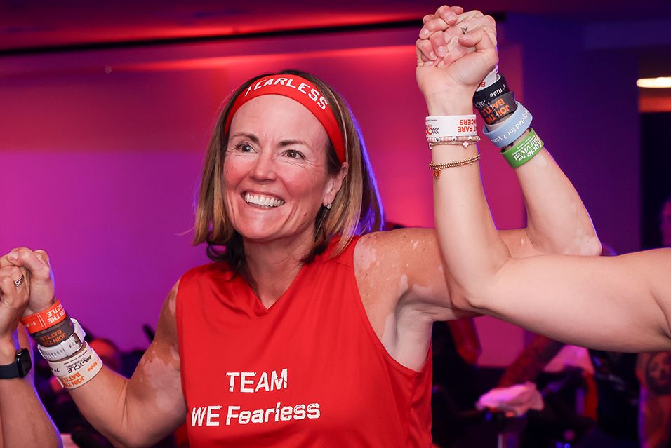 Smiling woman in red top and headband, holding hands with another in a celebratory pose.