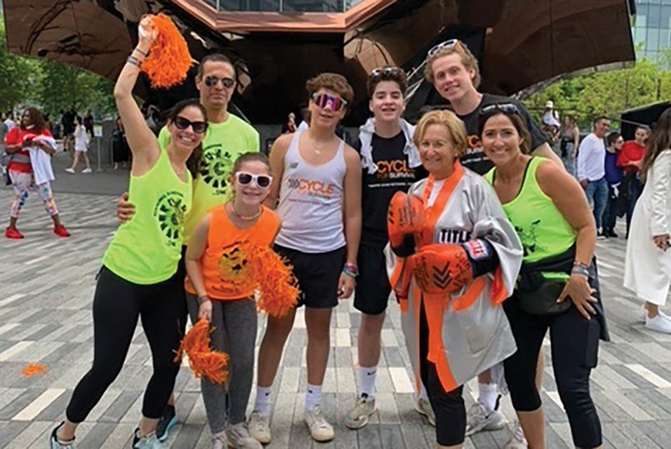 Group of people in athletic gear with orange pom-poms, outdoors on a plaza.