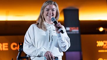 Cycle for Survival participant Jess Praley smiling and holding a microphone while giving a speech at a rare cancer fundraising event 