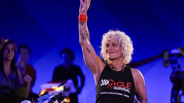 Individual leads Cycle for Survival event, raising arm with microphone, wearing MSK shirt, amid participants and stationary bikes. 