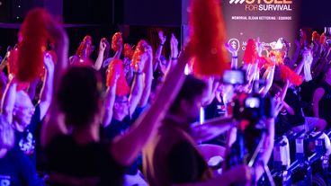 Riders raise orange pom-poms at Cycle for Survival with a banner for Cycle for Survival, Memorial Sloan Kettering, and Equinox behind. 