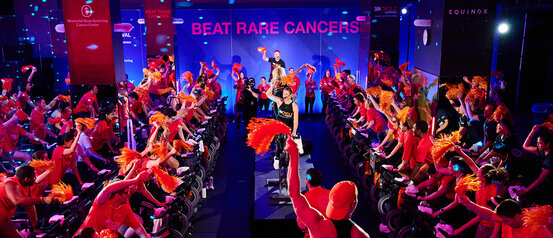 Cycling event with participants in red, raising orange pom-poms, vibrant atmosphere.