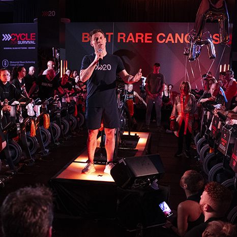Dave Linn addresses a crowd of participants on stationary bikes at a Cycle for Survival fundraising event for rare cancer research at MSK. 